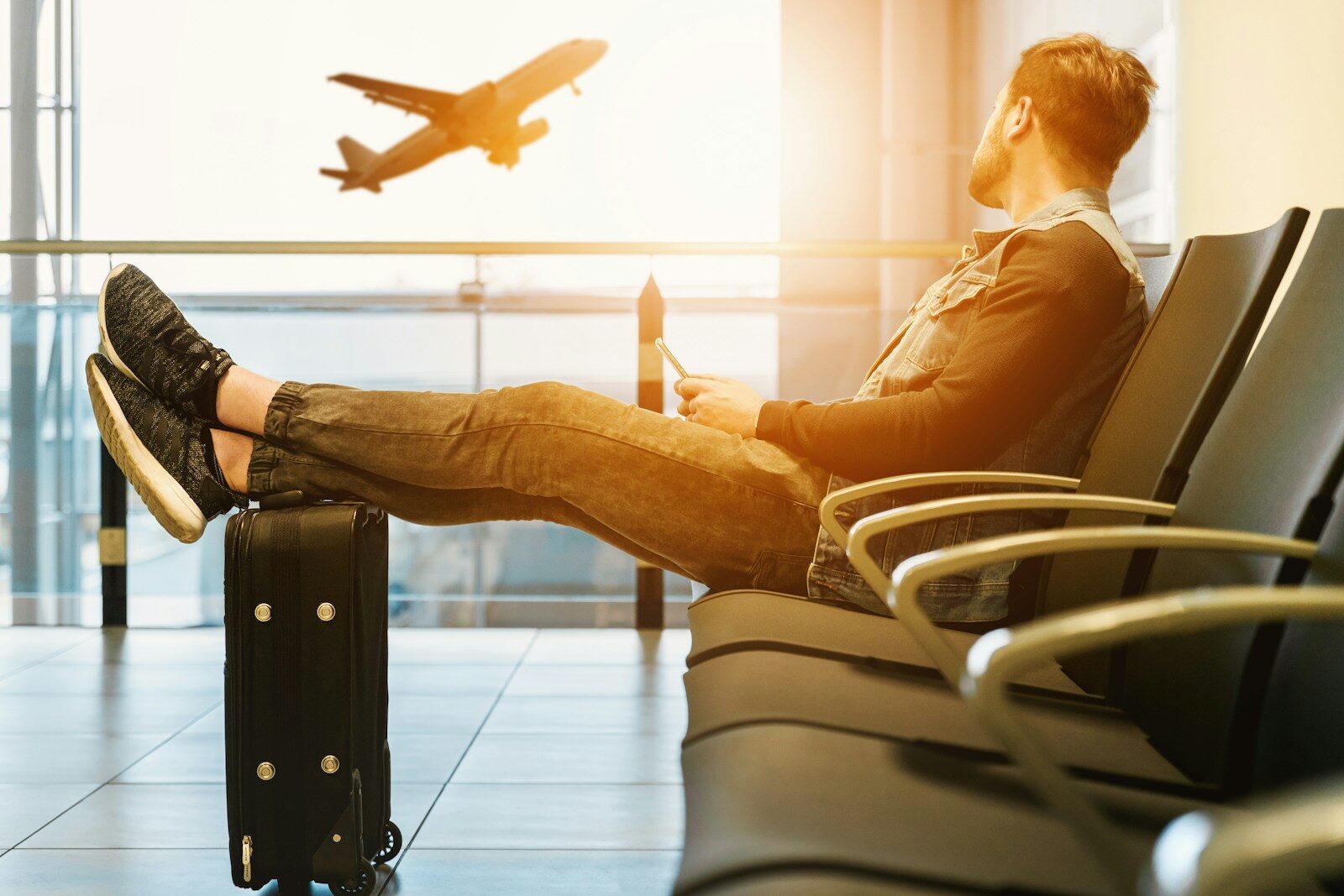 Photo by JESHOOTS.COM man sitting on gang chair with feet on luggage looking at airplane